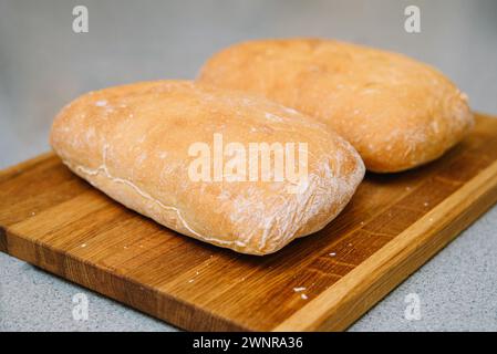 Two loaves of crusty ciabatta bread resting on a wooden cutting board, showcasing the art of traditional baking. Stock Photo