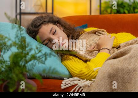 Tired 14-15 years Caucasian child girl lying down in bed taking a rest at home. Carefree teenager female kid napping falling asleep on comfortable sofa with pillows. Closed eyes enjoy daytime nap Stock Photo