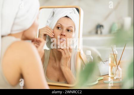 Middle-aged woman examining her facial skin looking in the mirror put on the table Stock Photo