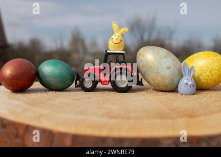 toy red tractor model stands on colorful Easter eggs laid in a row. Business concept for Easter greetings for farms. postcard. spring holiday Stock Photo