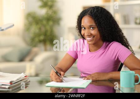 Happy black woman signing contract or filling form looks at you at home Stock Photo