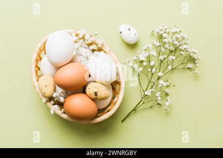 Happy Easter composition. Easter eggs in basket on colored table with gypsophila. Natural dyed colorful eggs background top view with copy space. Stock Photo