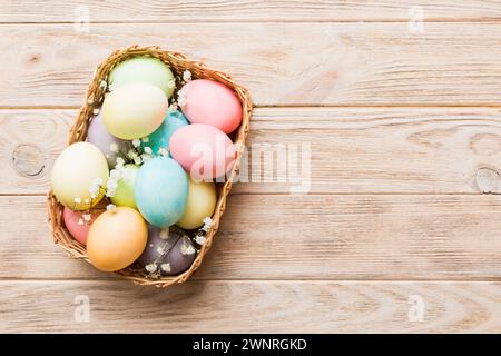Happy Easter composition. Easter eggs in basket on colored table with gypsophila. Natural dyed colorful eggs background top view with copy space. Stock Photo
