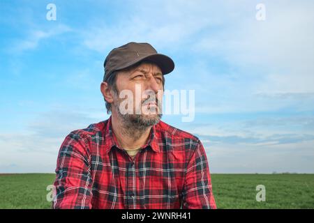 Portrait of mid-adult male farmer wearing brown cap and red plaid shirt in agricultural field, looking into distance, thinking and planning, selective Stock Photo
