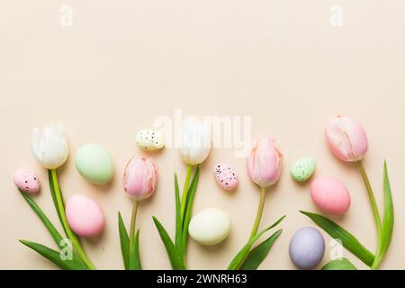 Happy Easter composition. Easter eggs on colored table with yellow Tulips. Natural dyed colorful eggs background top view with copy space. Stock Photo