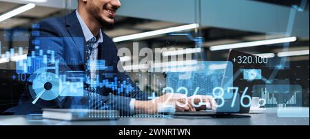 Smiling young professional working on a laptop in a modern office environment with futuristic holographic Stock Photo