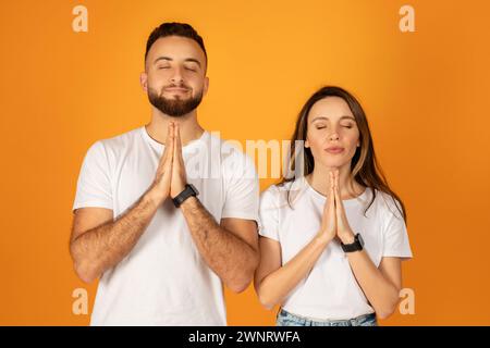 Peaceful young man and woman with eyes closed, hands pressed together in a prayer or meditative pose Stock Photo
