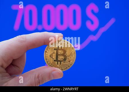 Bitcoin Münze zwischen Fingern vor einem Börsenkurs von über 70.000 USD *** Bitcoin coin between fingers in front of a market price of over 70,000 USD Deutschland, Germany GMS10914 Stock Photo