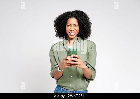 A young African-American woman in a green shirt beams as she holds her smartphone, embodying the connection between technology and daily joy Stock Photo