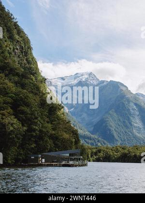 Dock with building hidden beneath tall green and snow capped mountains Stock Photo