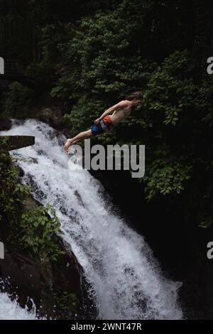 Man jumps from a cliff into the Alin-Alin waterfall. Bali Stock Photo