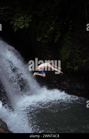 Man jumps from a cliff into the Alin-Alin waterfall. Bali Stock Photo