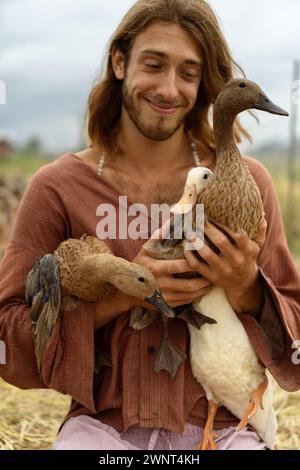 Happy long-haired man holds ducks in his hands. Stock Photo