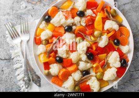 Festive Italian cauliflower salad with giardiniera, olives and anchovies close-up on a plate on the table. Horizontal top view from above Stock Photo