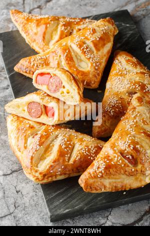 Pigs in blankets Sausage, cheese and peppers in puff pastry closeup on the marble board on the table. Vertical Stock Photo