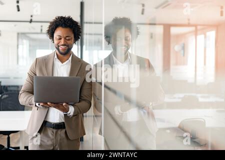 Professional businessman is immersed in laptop, smiling as he interacts with the content, encapsulating the joy of successful business endeavors and satisfaction of achieving goals in modern office Stock Photo
