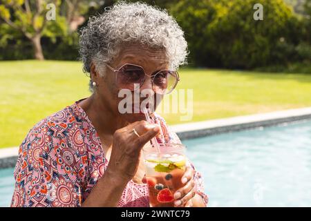 Senior biracial woman sips a drink by the pool Stock Photo
