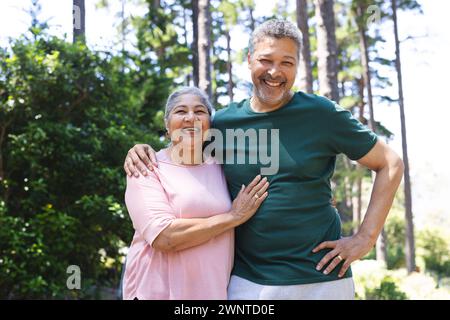 Senior biracial couple smiles warmly, standing outdoors with trees in the background Stock Photo