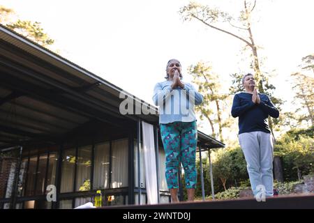 Senior biracial woman and biracial man practice yoga outdoors with copy space at home Stock Photo