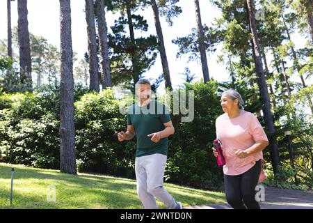 Senior biracial couple is jogging together in a sunny park Stock Photo