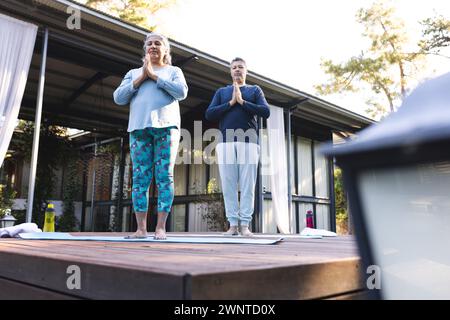 Senior biracial woman and biracial man practice yoga outdoors, at home Stock Photo