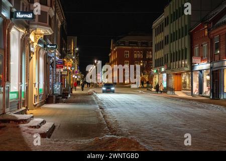 Night time street scene of main street in Tromso, with snow covered street and a car driving down it with pedestrians on the side walks. Stock Photo