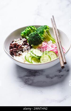 Vegan poke bowl with rice, broccoli, cucumber, beans and pickled red onion, white marble background. Stock Photo