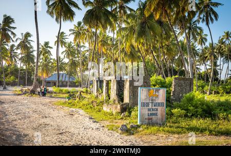 A ruined house, palm trees and sign for a beach lodge in Jambiani village, Zanzibar, Tanzania. Stock Photo