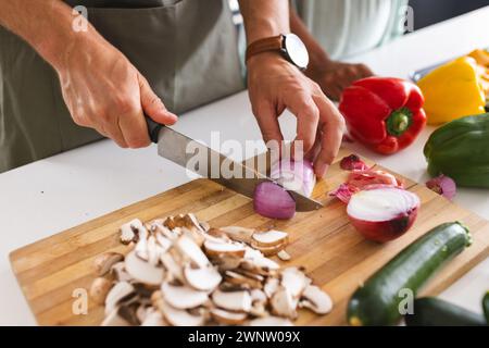 A person is chopping vegetables on a wooden cutting board in a kitchen Stock Photo