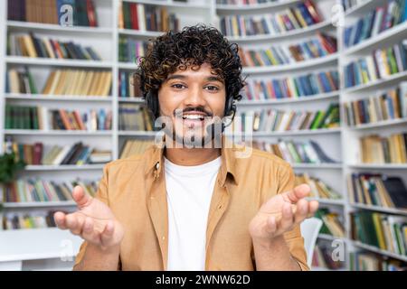 A young man in casual attire stands with an open gesture in a library setting, symbolizing concepts of choice, decision-making, education, and the vast world of knowledge. Stock Photo