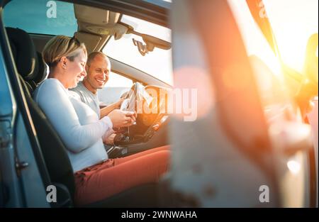 Happy smiling two young adulds couple using smartphone navigation inside car during auto jorney.They are laughing during road trip. Family, couples re Stock Photo