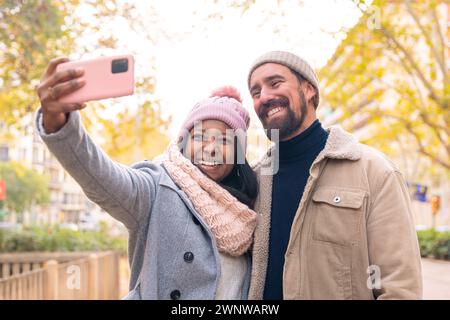 Multiethnic smiling young couple making selfie on cell phone outdoors. Stock Photo