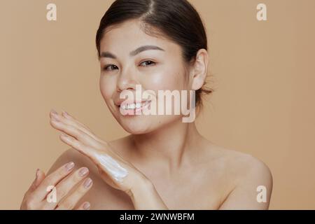 Portrait of modern asian female with hand cream isolated on beige background. Stock Photo