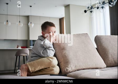 Cute little boy curiously looking at something. Curious kid full of interest watching his favorite show. Adorable child lying on couch in living room and relaxing. Stock Photo