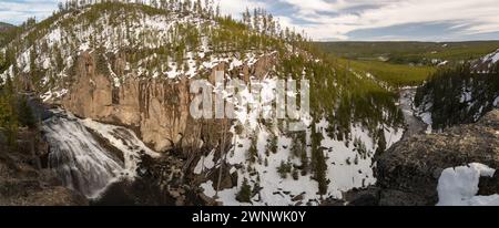 An enchanting image of a powerful waterfall cascading through a snow-covered landscape, cutting through the rugged cliffs surrounded by pine trees Stock Photo