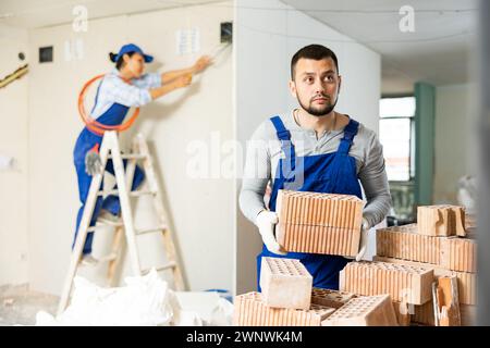 Repairman in coverall carrying bricks during apartment renovation Stock Photo