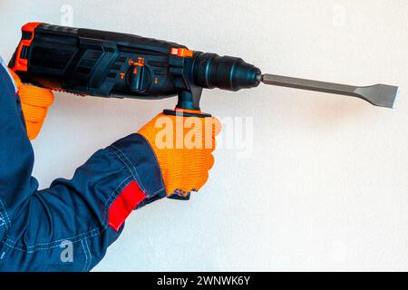 workman with a rotary hammer. Hands in protective gloves with hammer drill perforator. Copy space. Stock Photo
