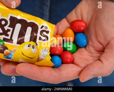 Tambov, Russian Federation - January 23, 2024 Woman pouring M&Ms candies into her hand from a packet. Close-up Stock Photo