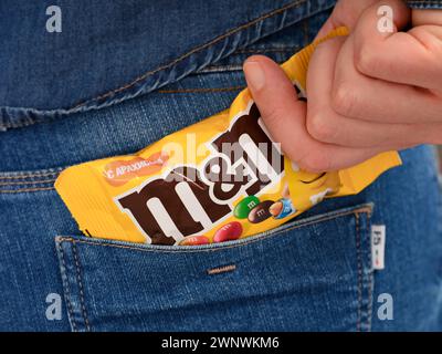 Tambov, Russian Federation - January 23, 2024 A woman hand taking out M&Ms pack of a jeans back pocket. Stock Photo