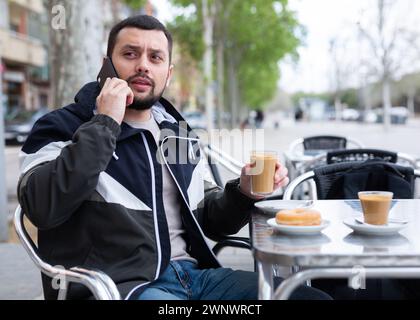 Young man talking on phone during breakfast in street cafe Stock Photo