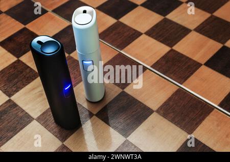 Electronic cigarette technology. Top view of two electric hybrid cigarettes tobacco heating system in white and blue housing on a chessboard Stock Photo