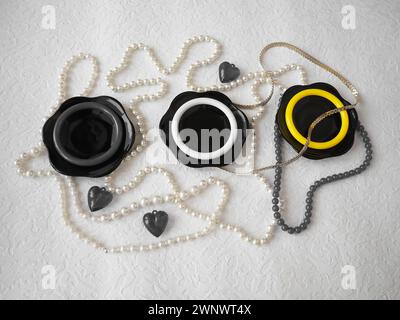 Flat lay. A beautiful composition of glass black dishes, plastic jewelry, bracelets, beads, hearts on a white background. Women's baubles for February Stock Photo