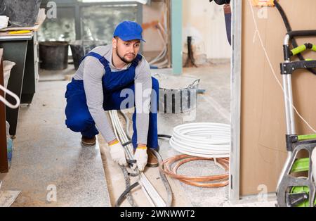 Man electrical installer laying cables through trench Stock Photo