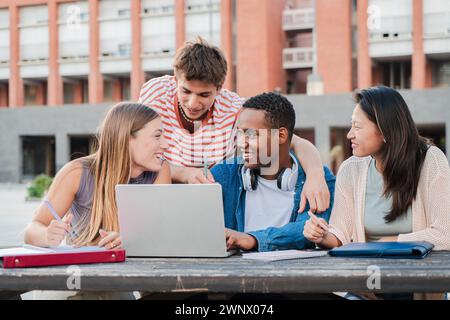 Group of multiracial happy teenage students using laptop, working on university assignment homework project at university campus. Meeting of diverse young classmates looking information on computer. High quality photo Stock Photo
