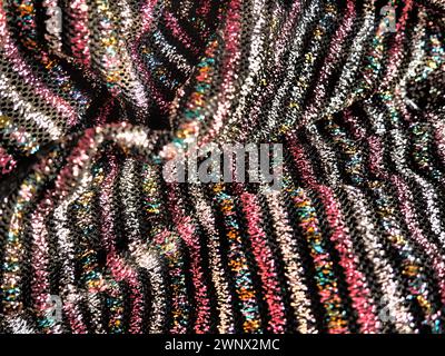 Cloth with lurex. Striped elegant knitted textiles with pink, red, silver and gold stripes on a black background. Burning cloth, carelessly folded by Stock Photo
