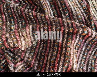 Cloth with lurex. Striped elegant knitted textiles with pink, red, silver and gold stripes on a black background. Burning cloth, carelessly folded by Stock Photo