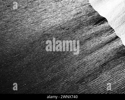 Black or gray corrugated paper. Uneven surface. Abstract monochrome background. Wavy edges of the paper sheet. Lighting gradient. Corrugated texture Stock Photo