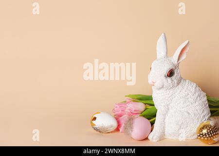 Happy Easter. Congratulatory beige Easter background with bunny, eggs and tulips, copy space Stock Photo