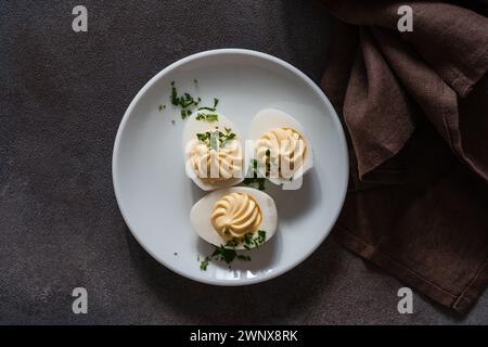 Healthy deviled eggs topped with fresh herbs on white plate, perfect Easter party appetizer, high angle view Stock Photo