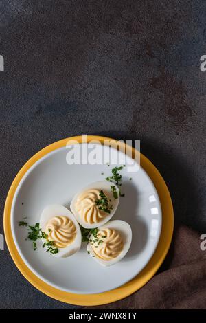 Healthy deviled eggs topped with fresh herbs on white plate, perfect Easter party appetizer, high angle view, copy space Stock Photo